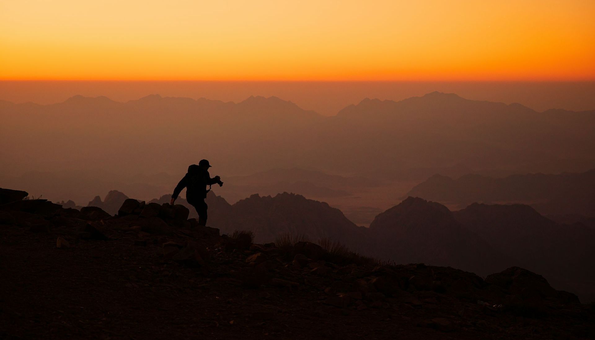 Someone climbing a mountain with the sun setting in the background.
