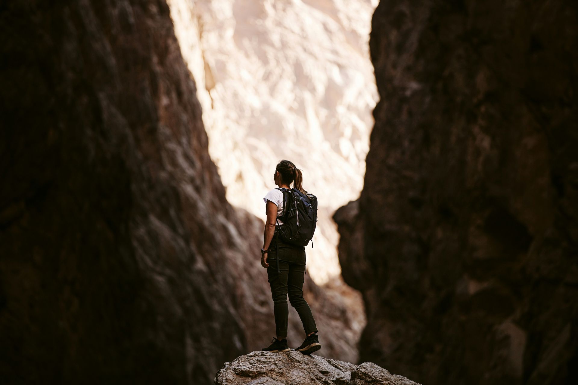 A woman hiking in a desert with the sun in the background.