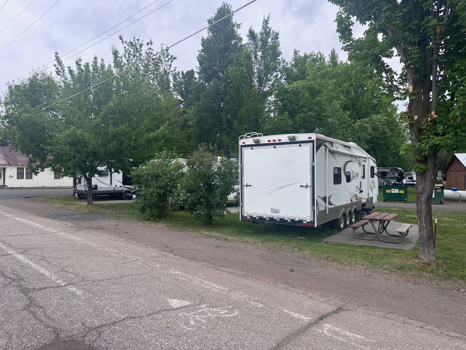 A white trailer is parked on the side of the road next to a picnic table.