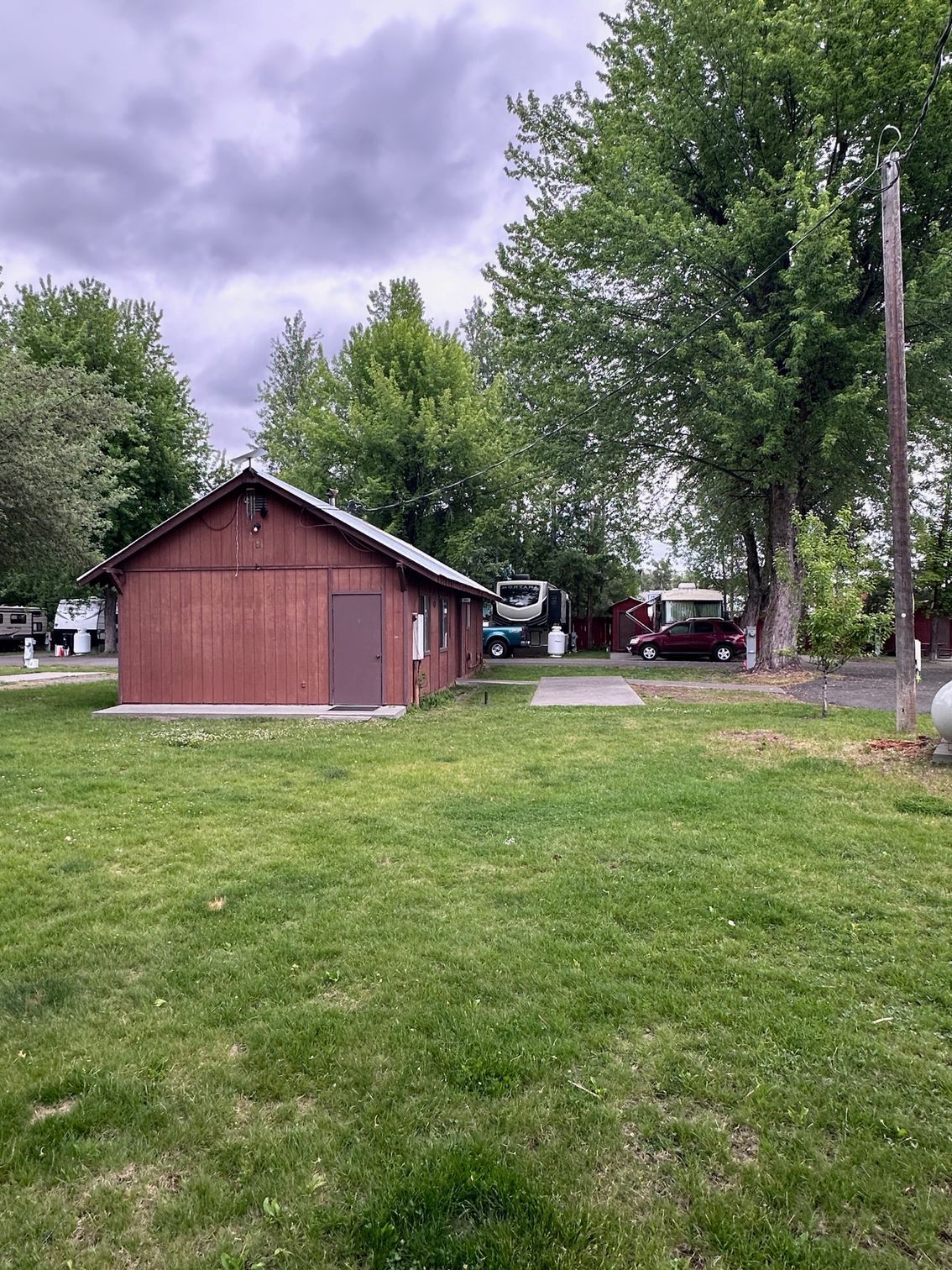 A small wooden building is sitting in the middle of a lush green field.