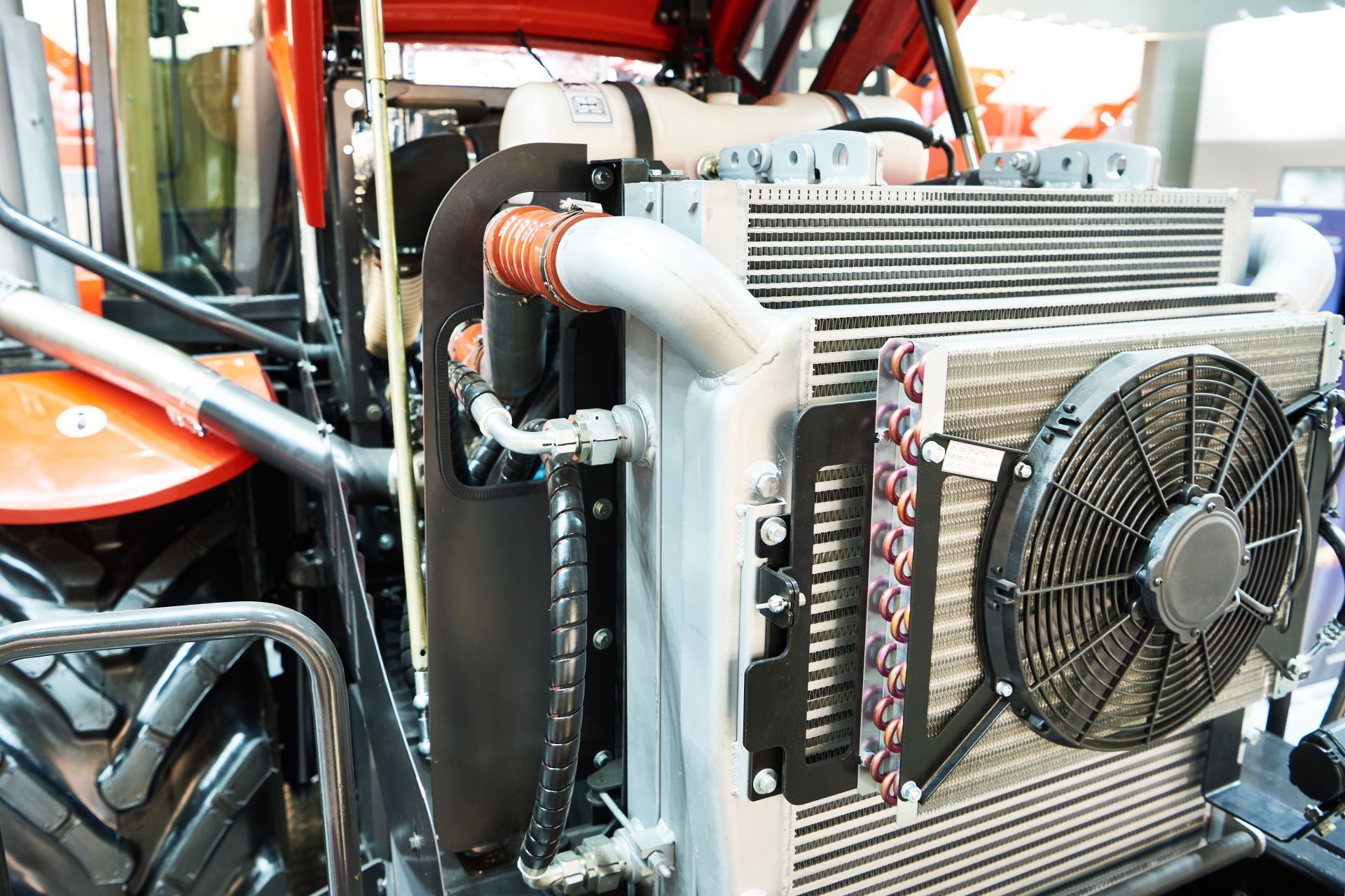 Close-up of a tractor's engine cooling system with a radiator, fan, and orange tubing.