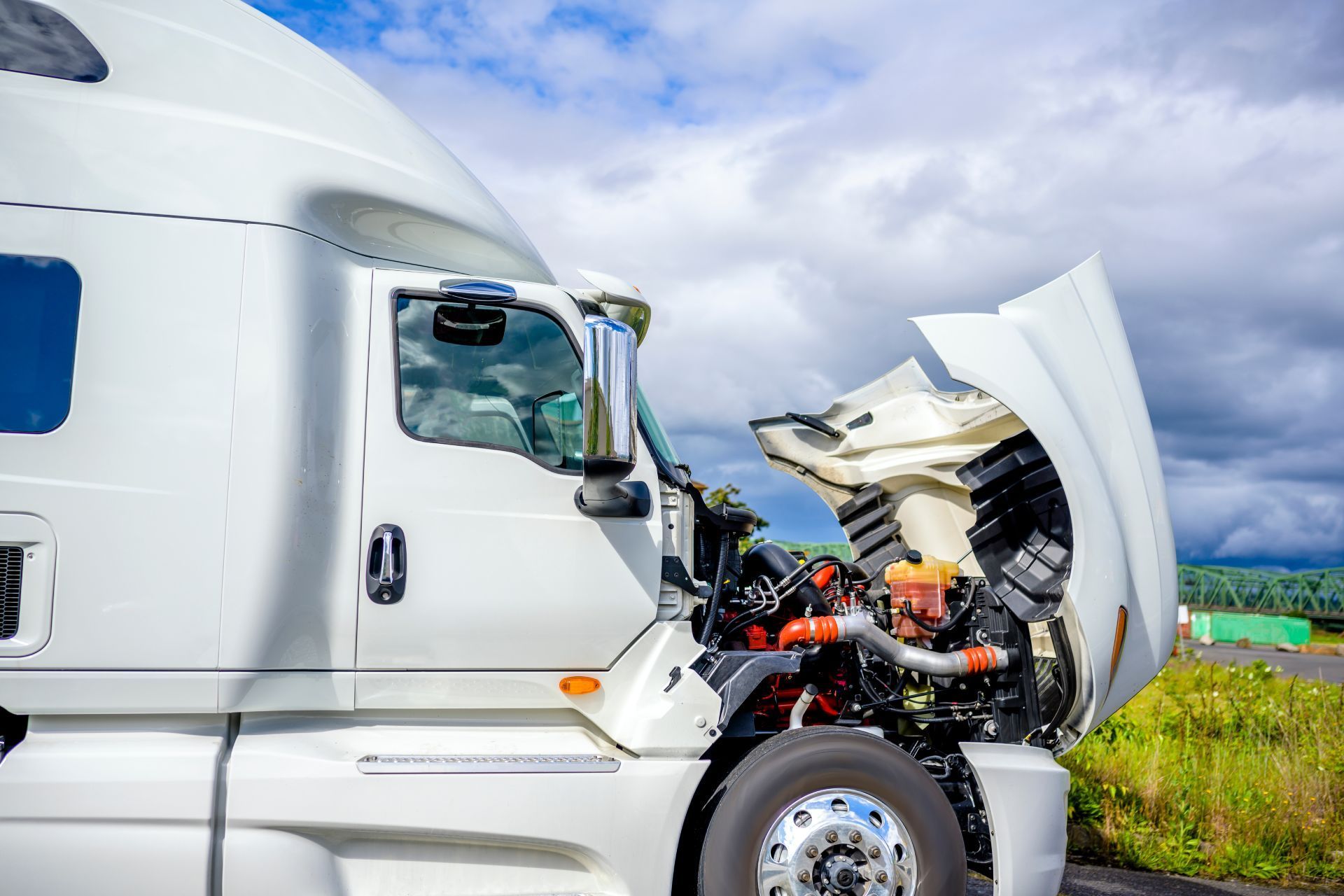 White semi-truck with open hood; engine visible. Outdoors, cloudy sky.