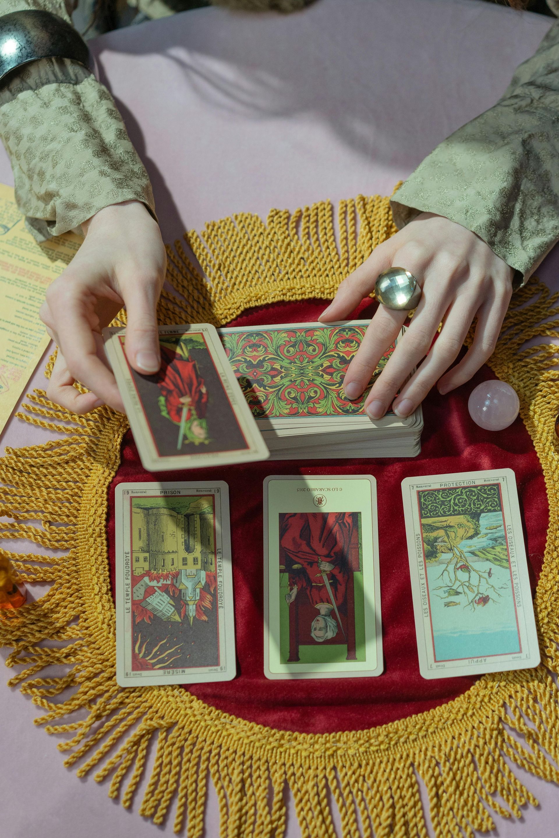 Person shuffling tarot cards; a spread of three cards is visible on a table with a gold fringed cloth.