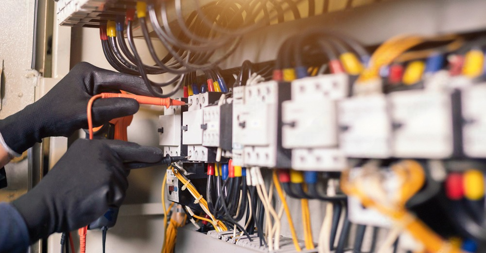 An electrician is working on an electrical panel with a multimeter.