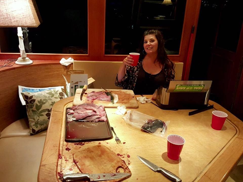 Woman seated, holding red cup, next to a table with carved meat and red cups.