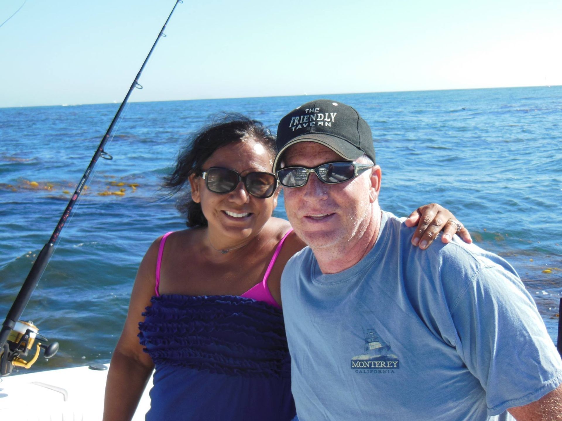 Woman and man on a boat, smiling, with ocean in background and fishing rod.