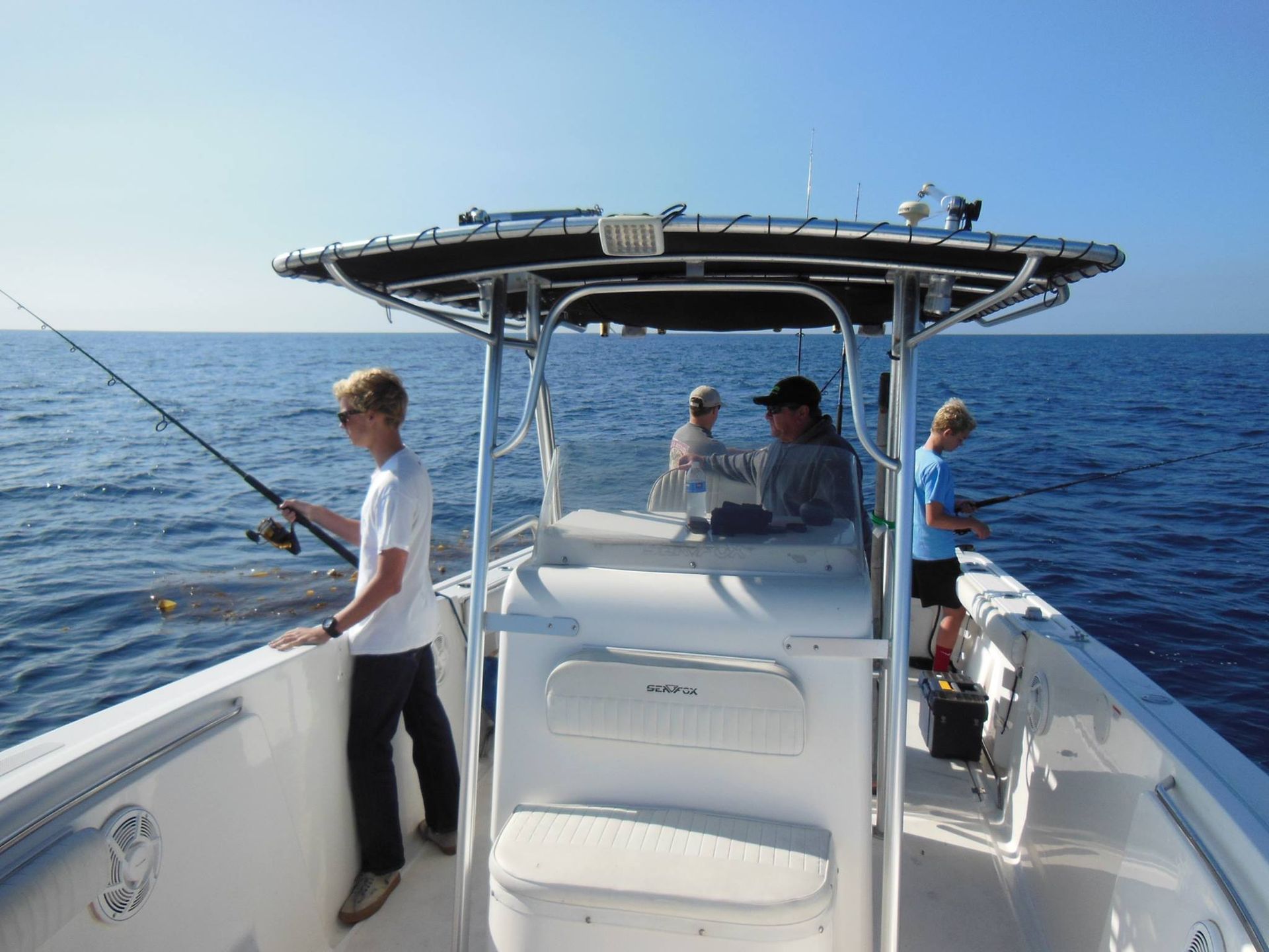 People fishing from a white boat on the ocean under a clear sky.