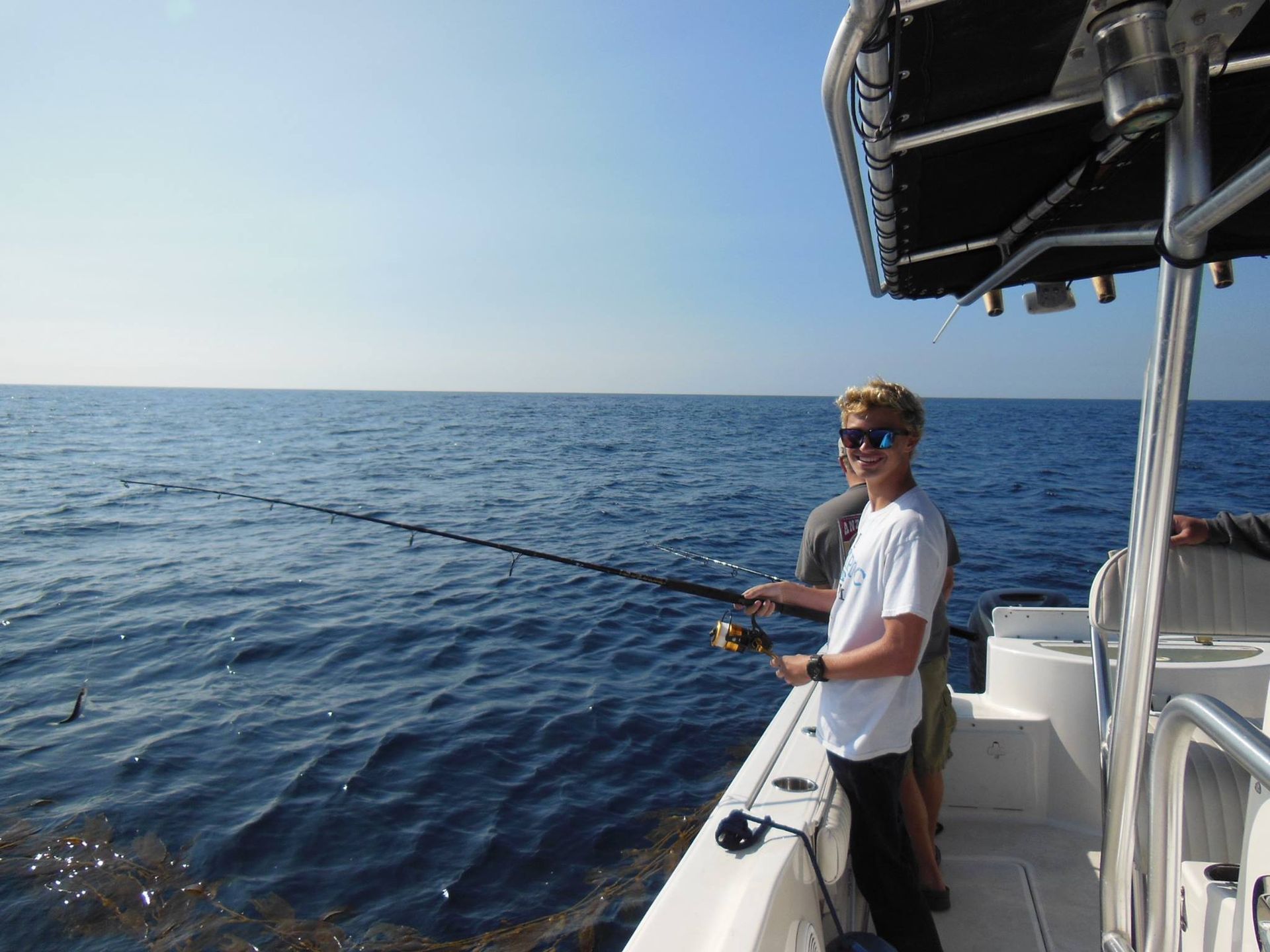 Boy fishing from a boat on a sunny day. He holds a fishing rod, looking out at the water.