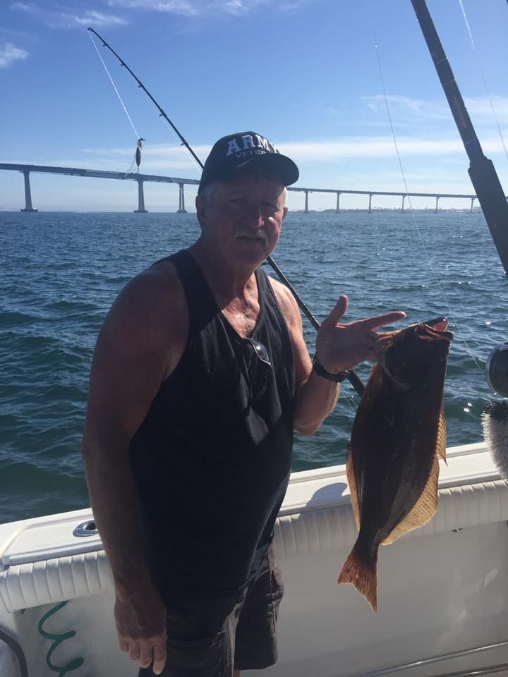 Man on a boat holding a fish, with a bridge in the background. Sunny day.