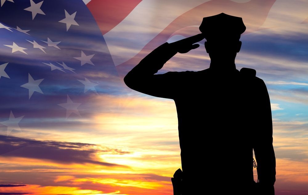 Silhouette of a saluting soldier against an American flag and sunset.