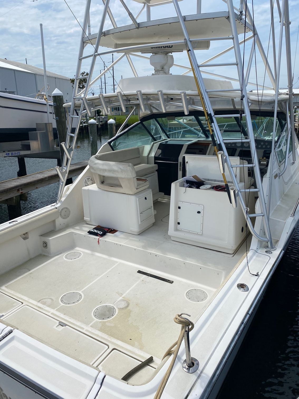 The cockpit and helm of a white sportfishing boat docked at a marina under a bright, cloudy sky.