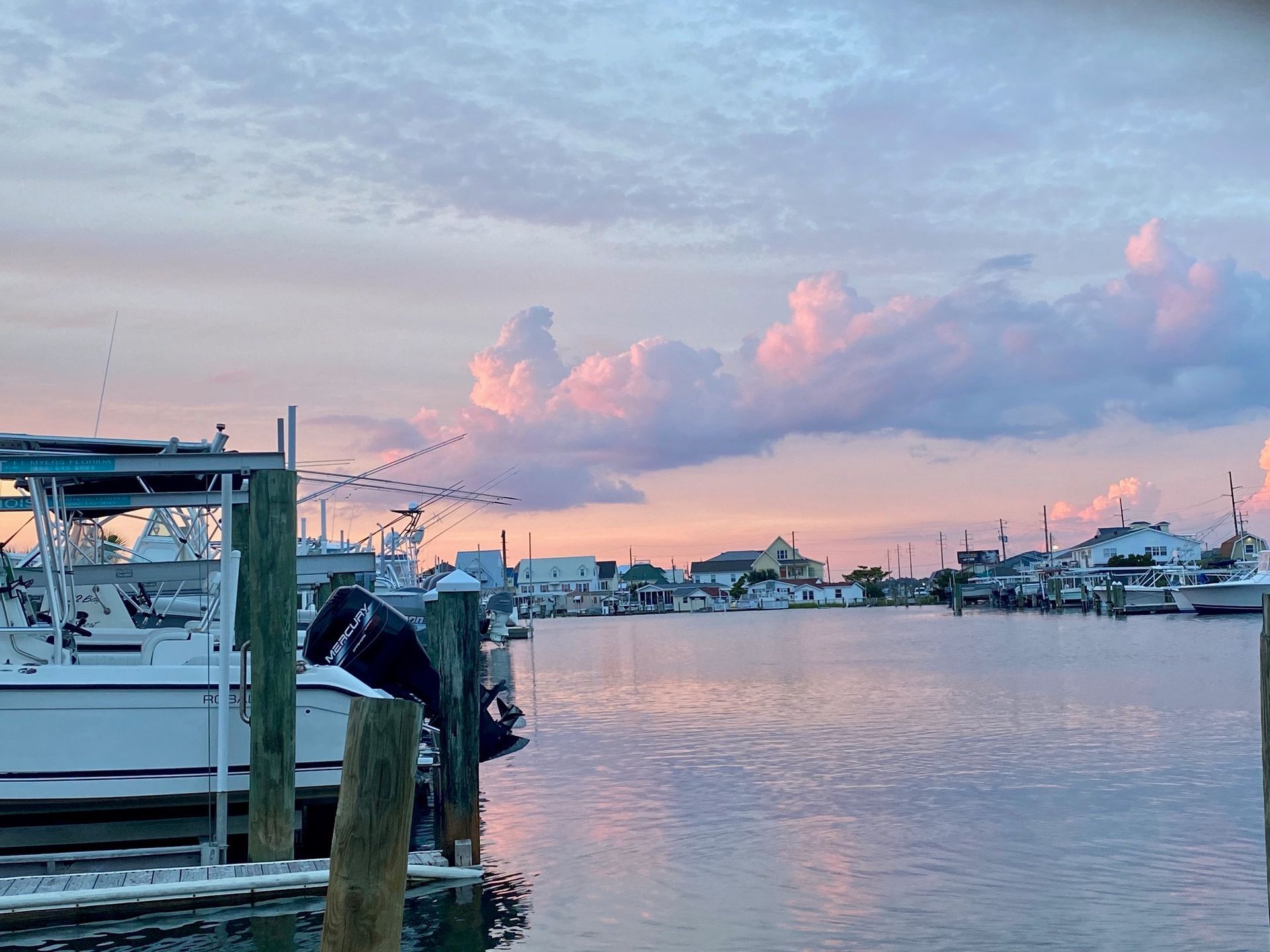 Boats docked at a marina during a sunset with pink and blue clouds reflecting on the water.