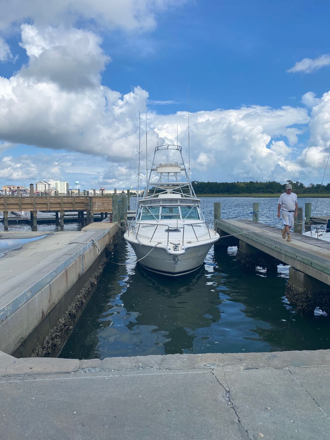 A white sportfishing boat moored in a narrow slip at a dock under a partly cloudy sky.