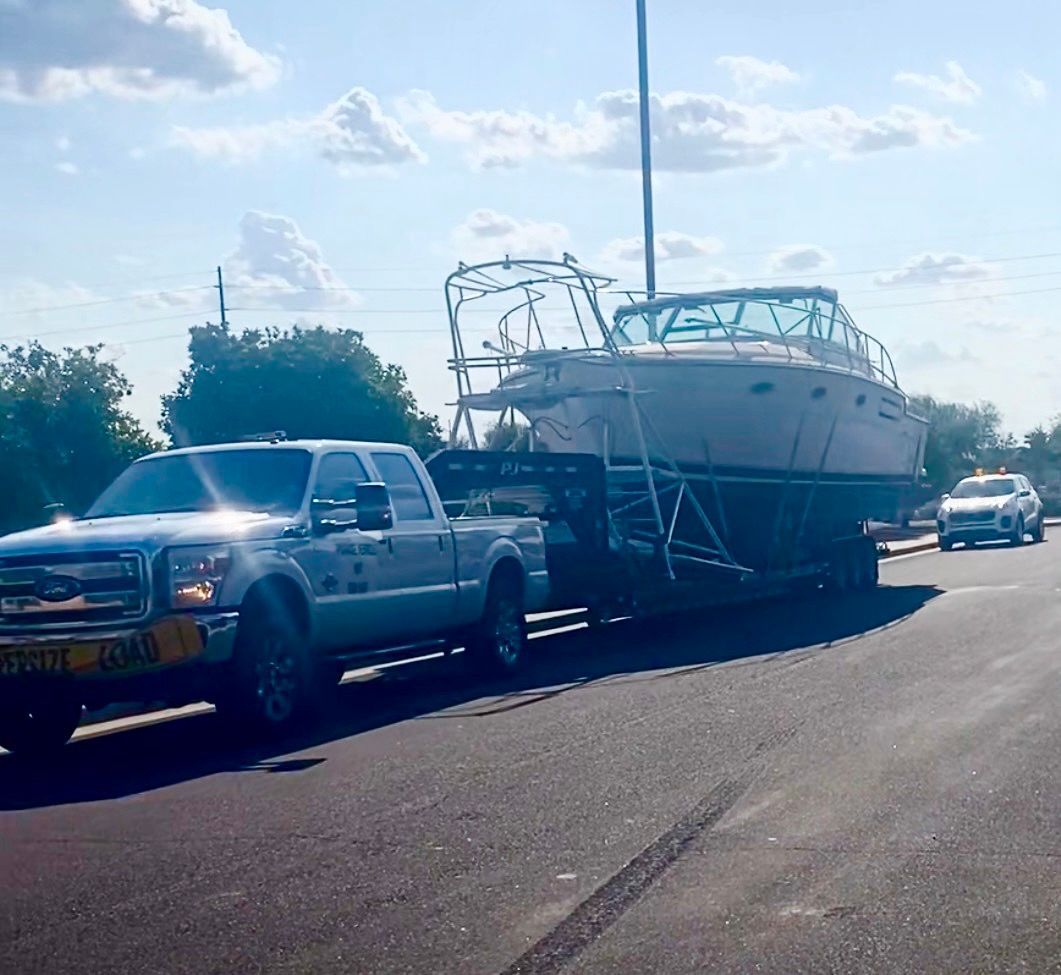 A silver pickup truck hauls a white boat on a trailer along a sunny road.