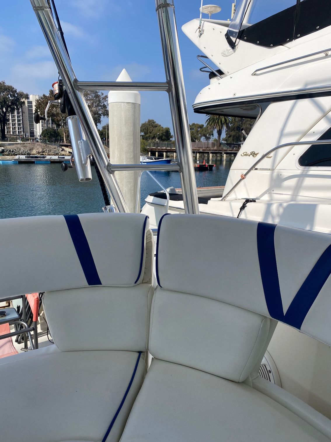 White padded bench seats with blue accents on the deck of a boat, overlooking a marina with boats and palm trees.