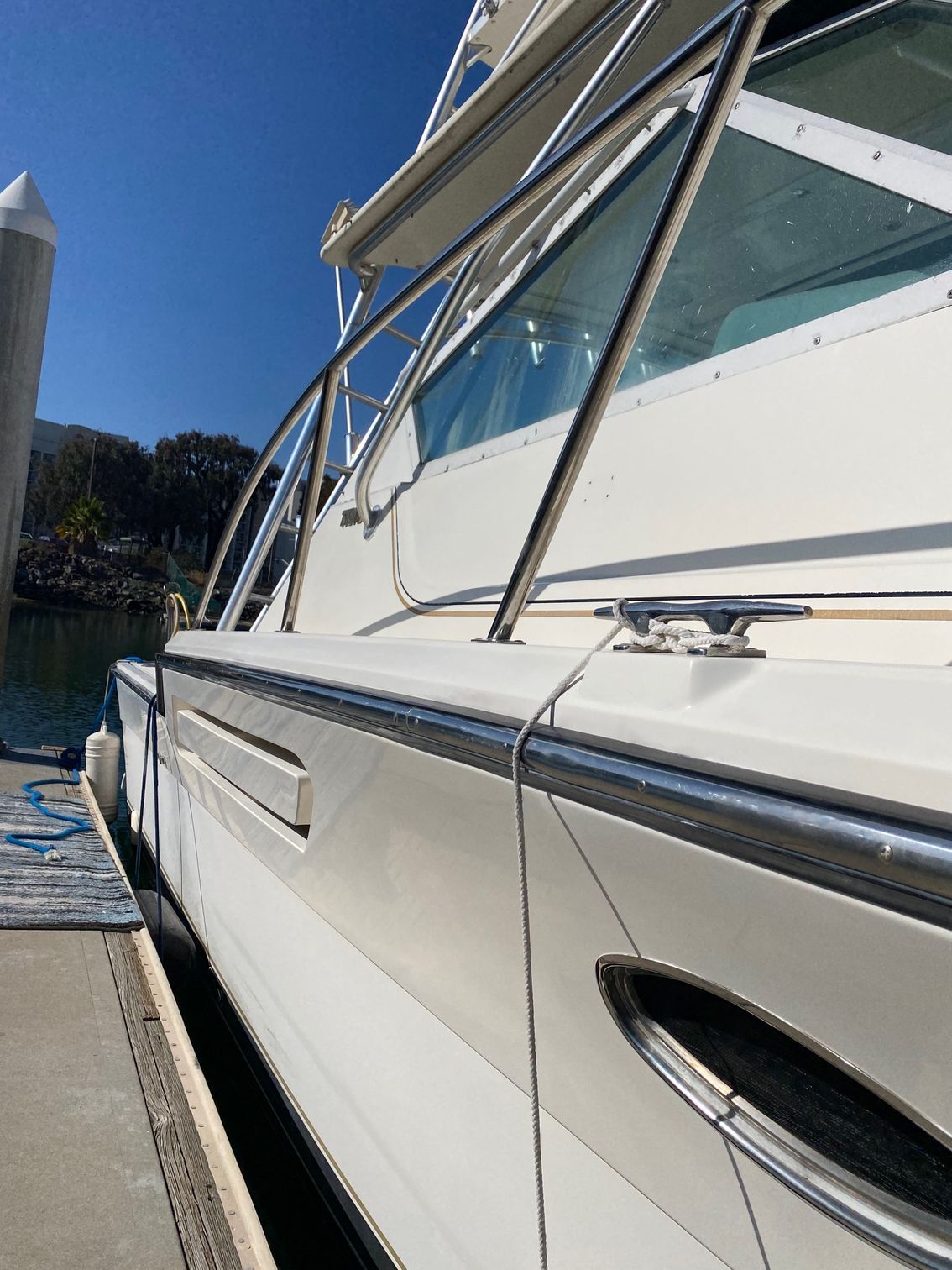 A close-up, low-angle view of a white boat hull docked next to a concrete pier on a sunny day.
