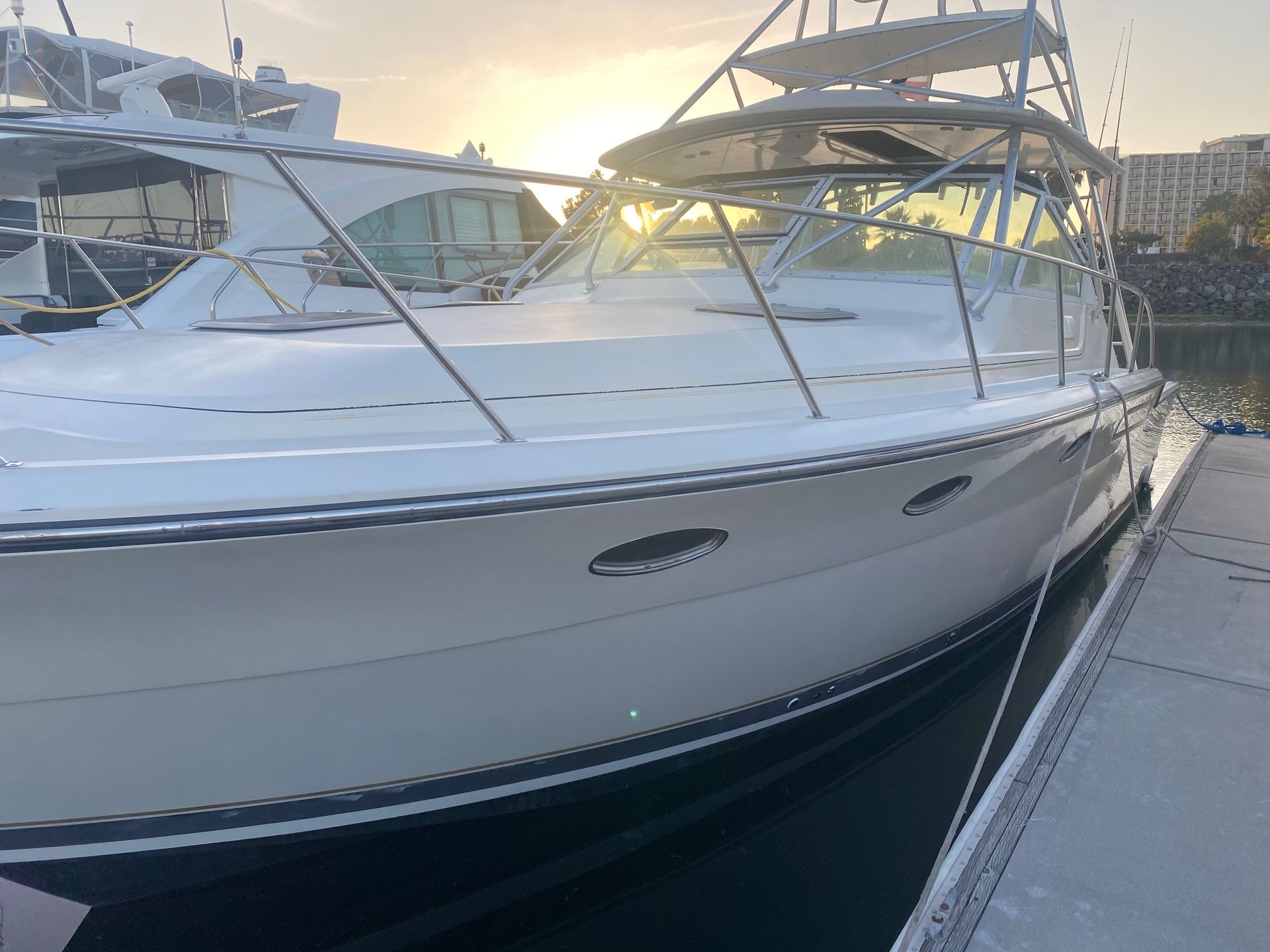 A white sport fishing yacht docked in a marina at sunset, with a golden sun glowing over the cabin top.