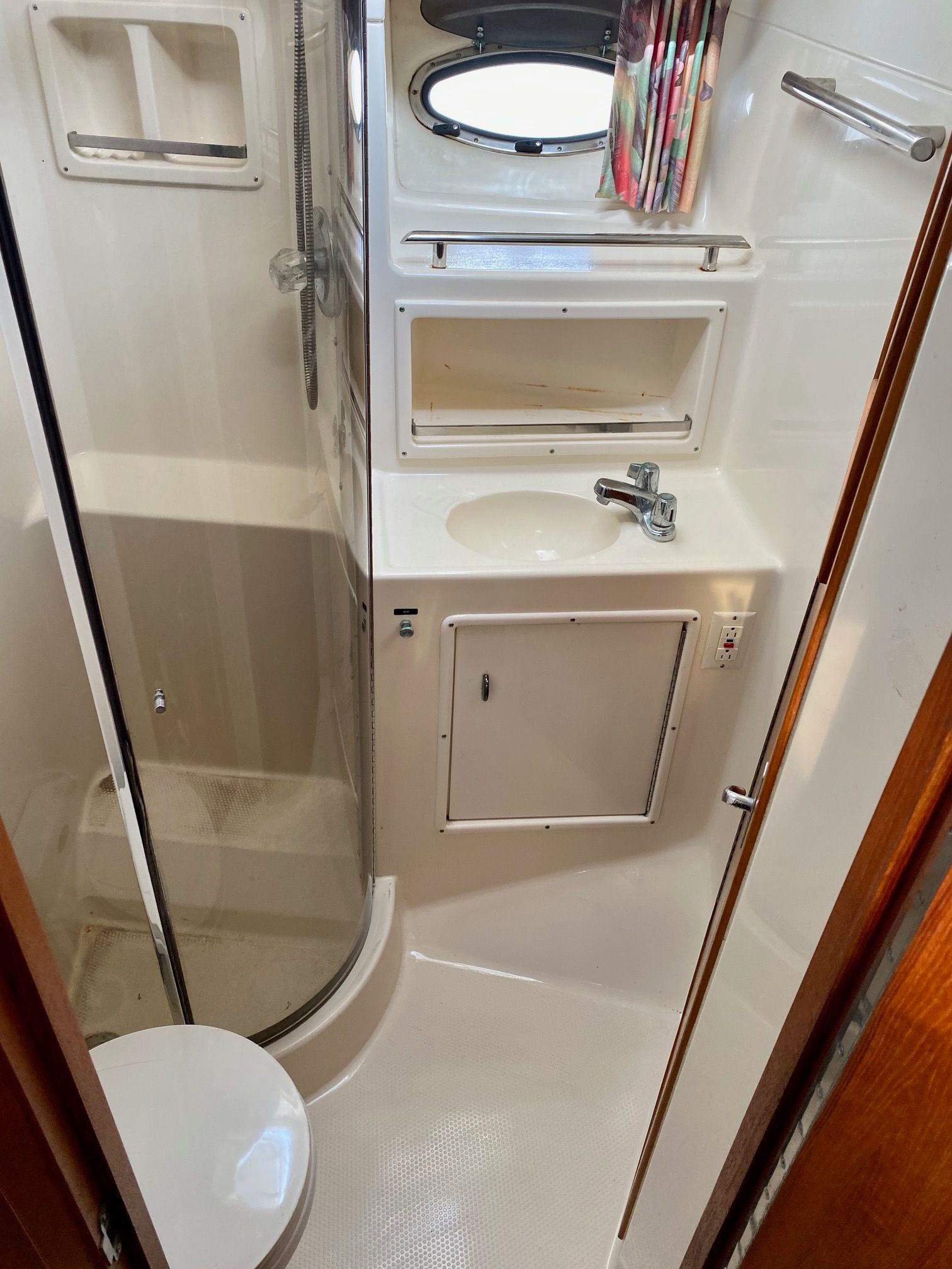 Small, white, compact marine bathroom featuring a corner shower stall, a small sink with a vanity, and a round toilet.