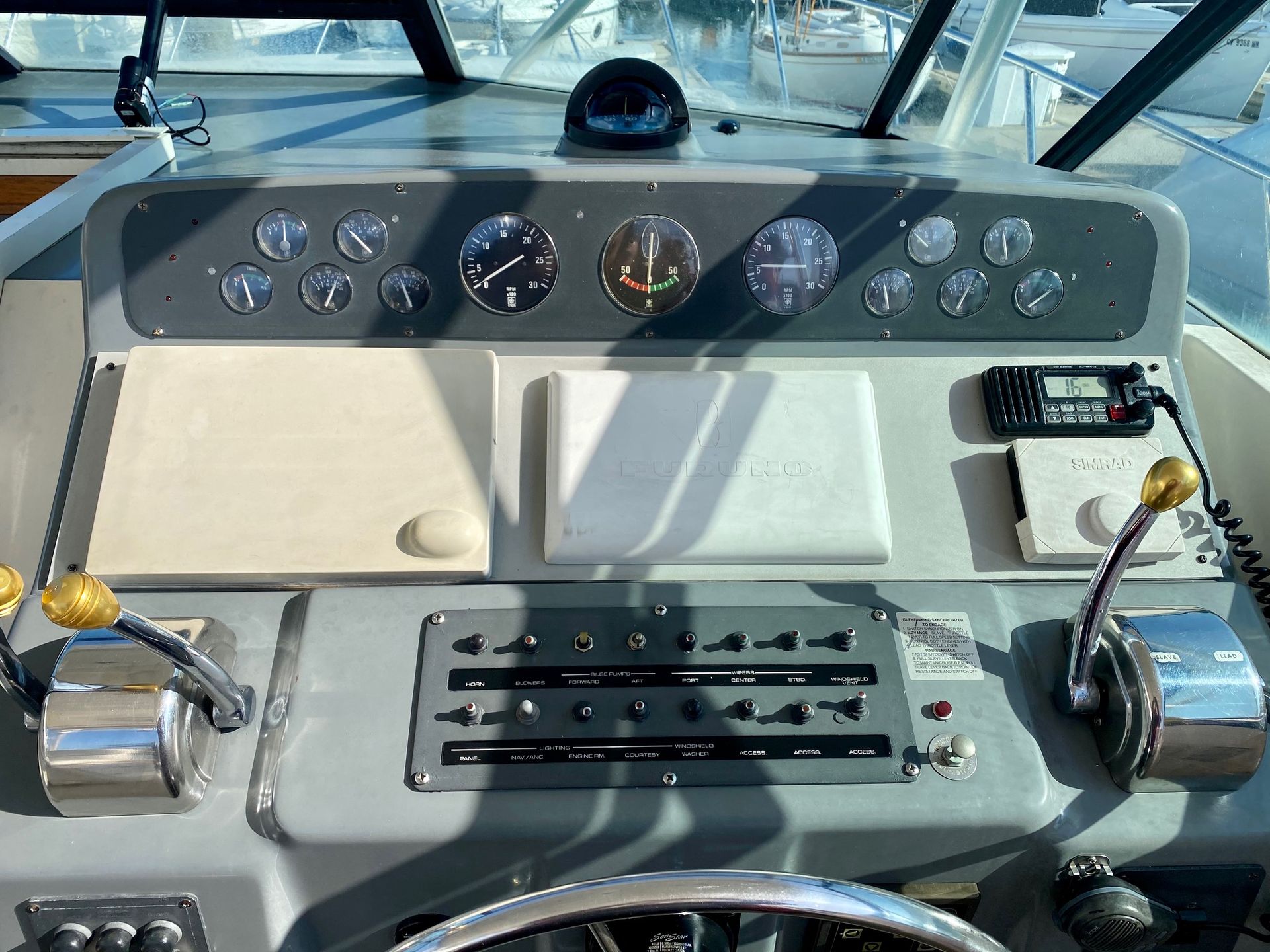 The cockpit of a boat featuring a grey dashboard with various gauges, a VHF radio, and two chrome throttle levers.