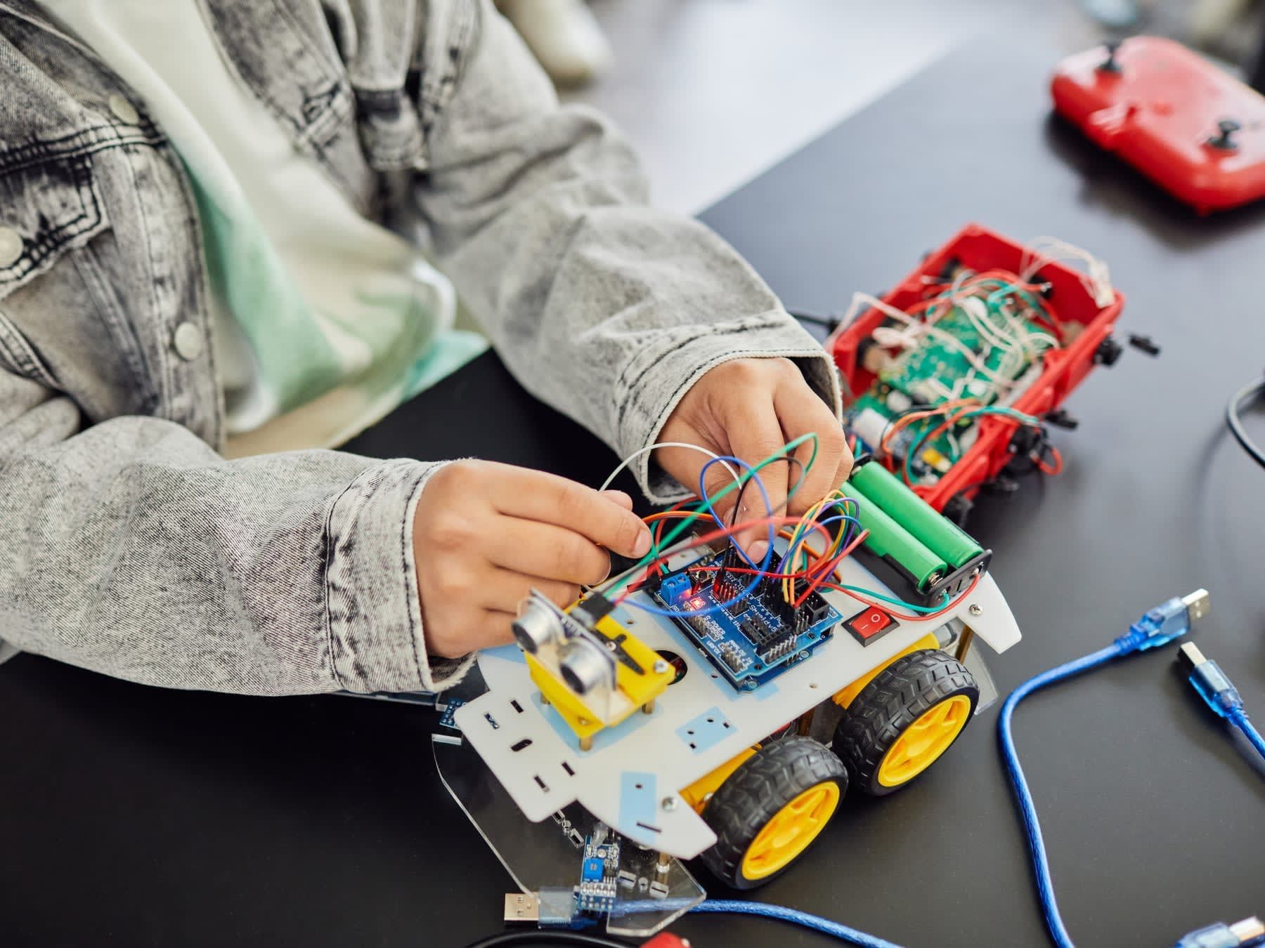 Person assembling a small robot car with wires and electronic components.