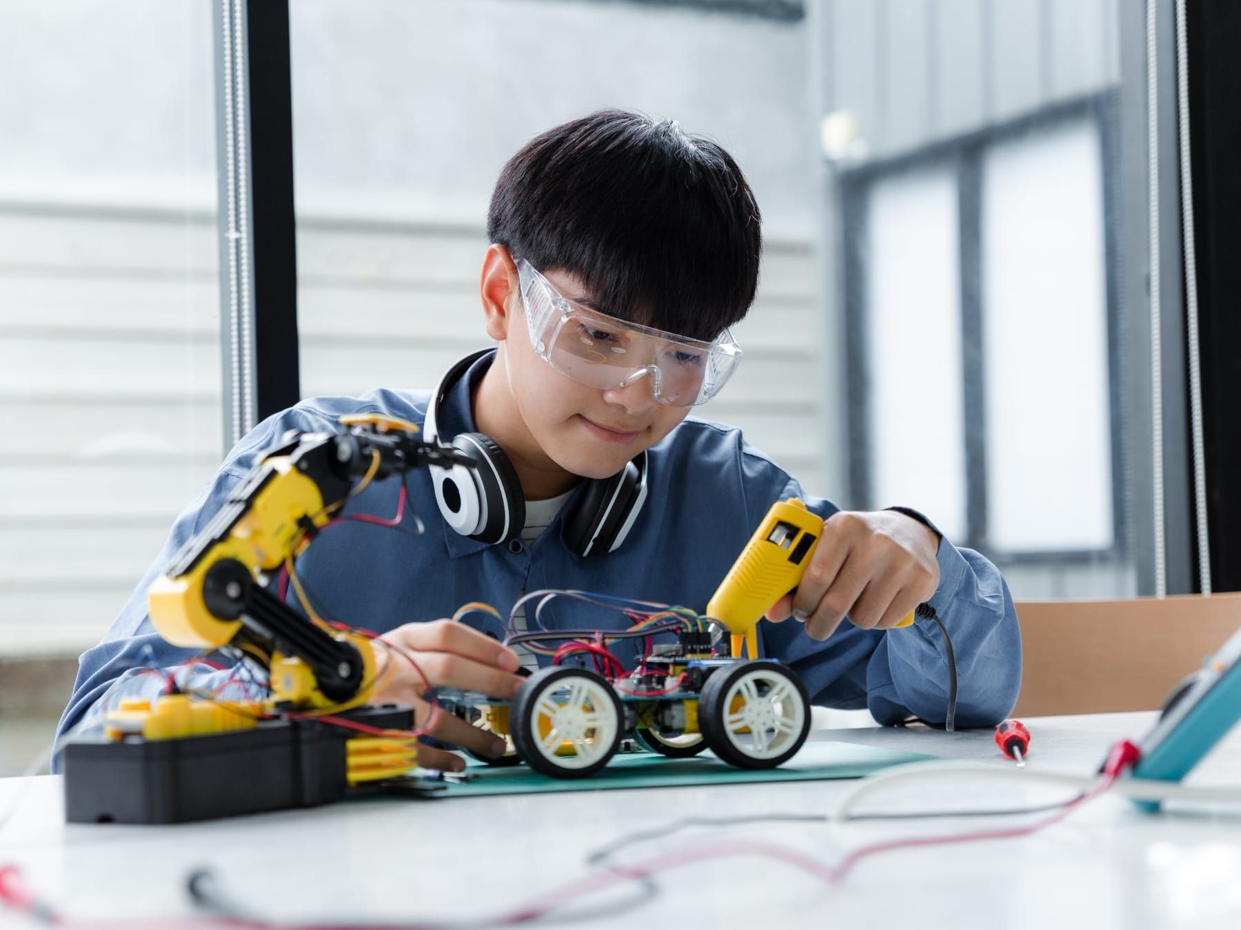 Young person with safety glasses soldering a robot car, indoors.