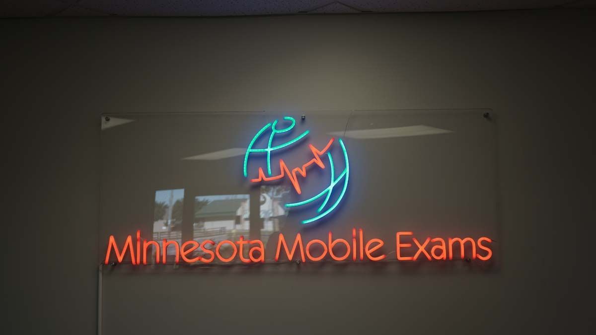 A neon sign for minnesota mobile exams hangs on a wall.