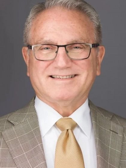 A man wearing glasses and a suit and tie smiles for the camera