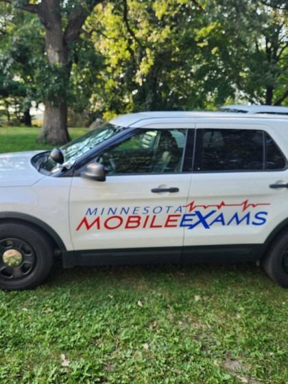 A white minnesota mobile exams car is parked in the grass.