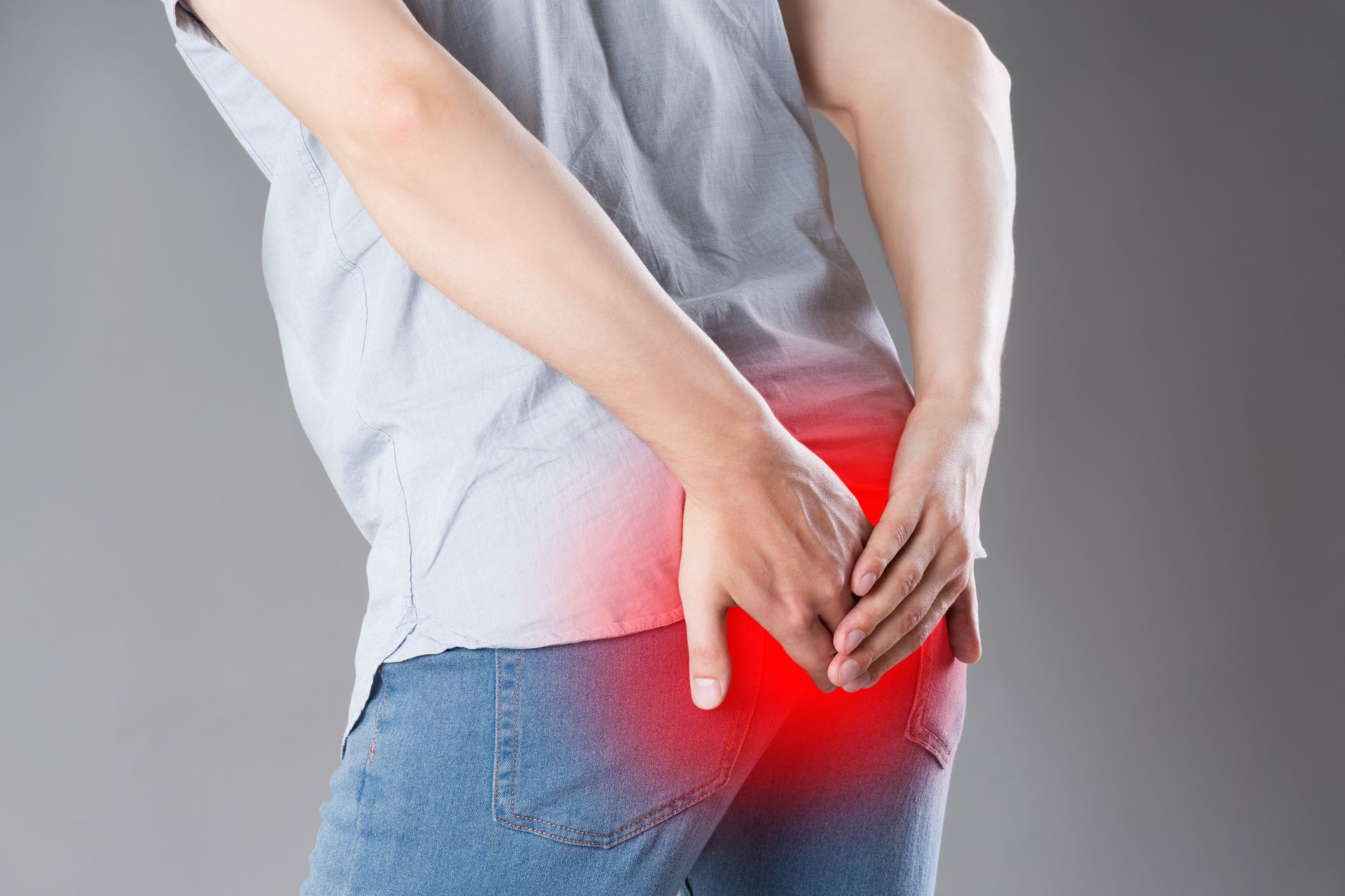 Person holding their hand over their reddened buttock, indicating pain. Gray background.