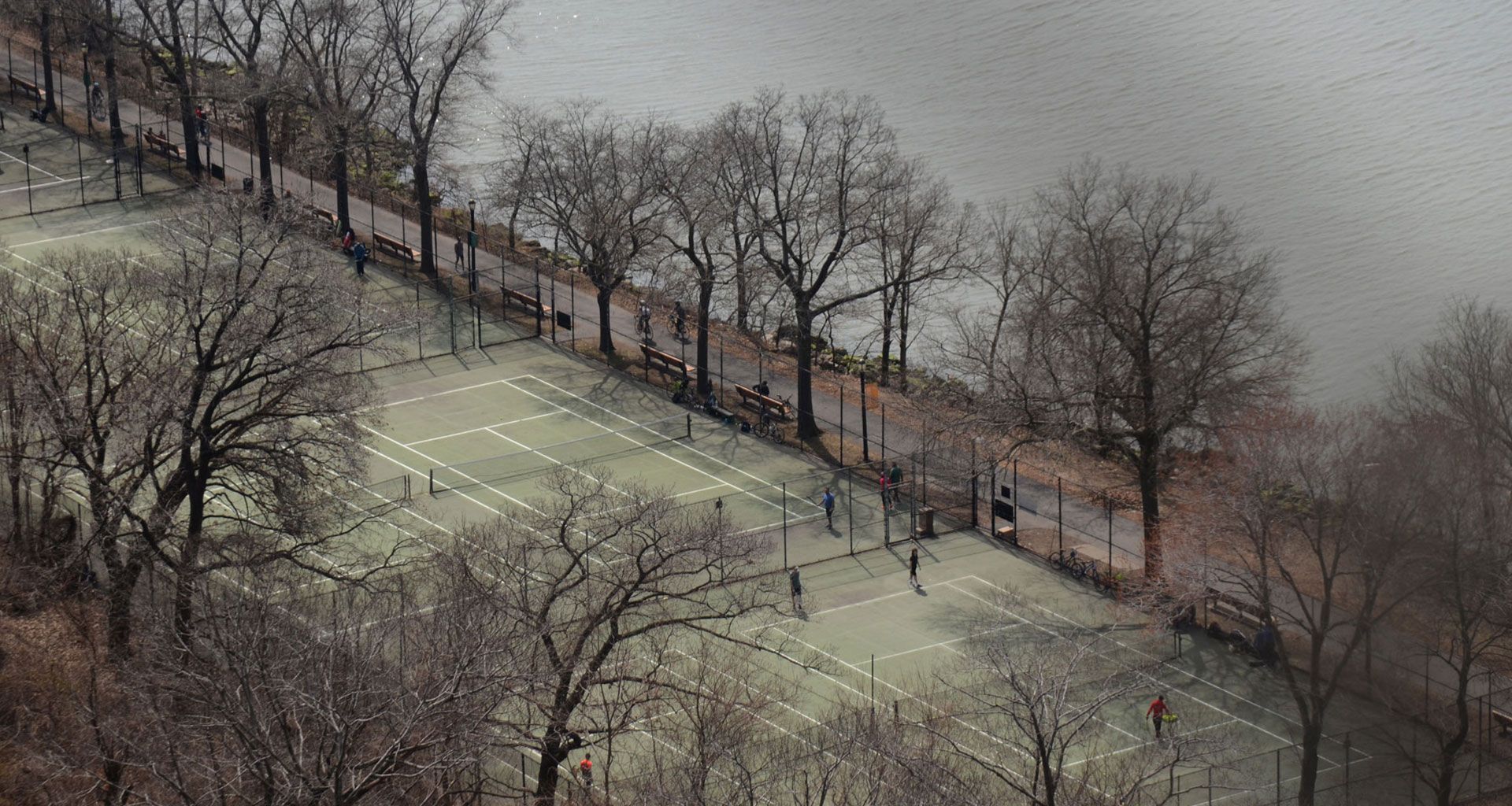 An aerial view of a tennis court surrounded by trees and a body of water.