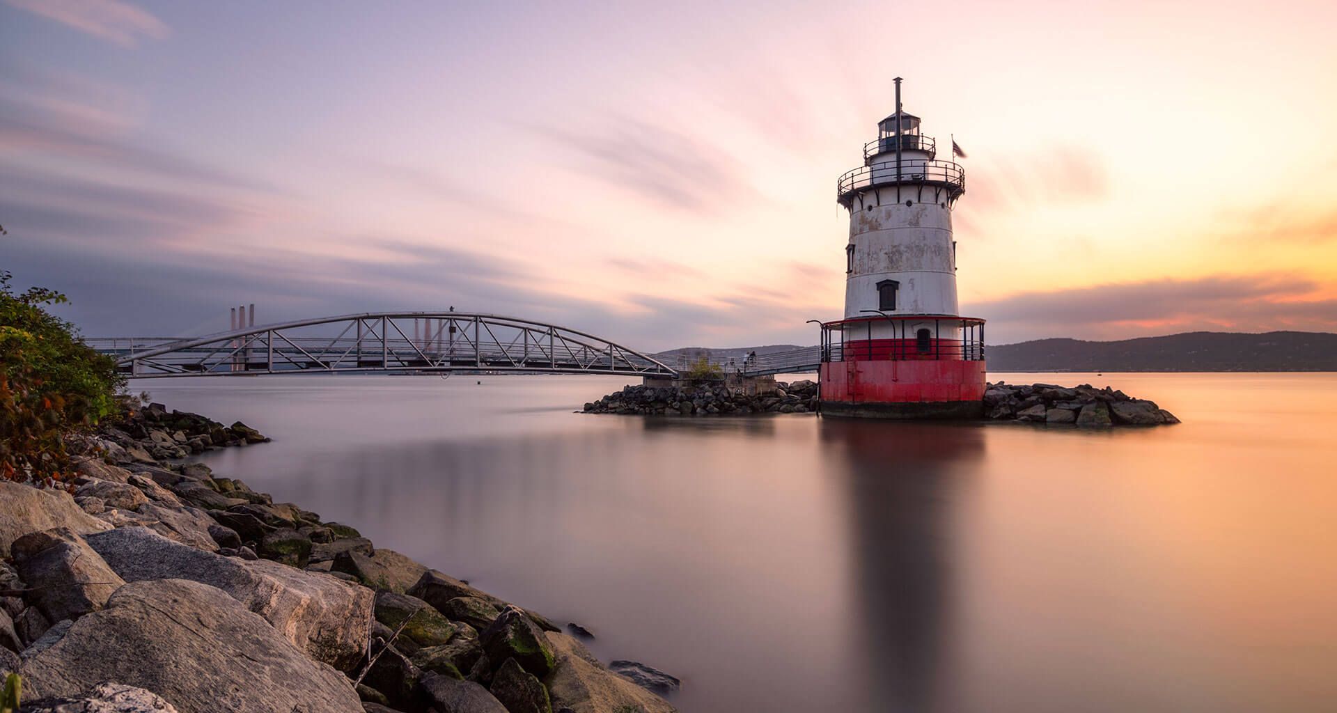 A lighthouse is sitting on a small island in the middle of a body of water.