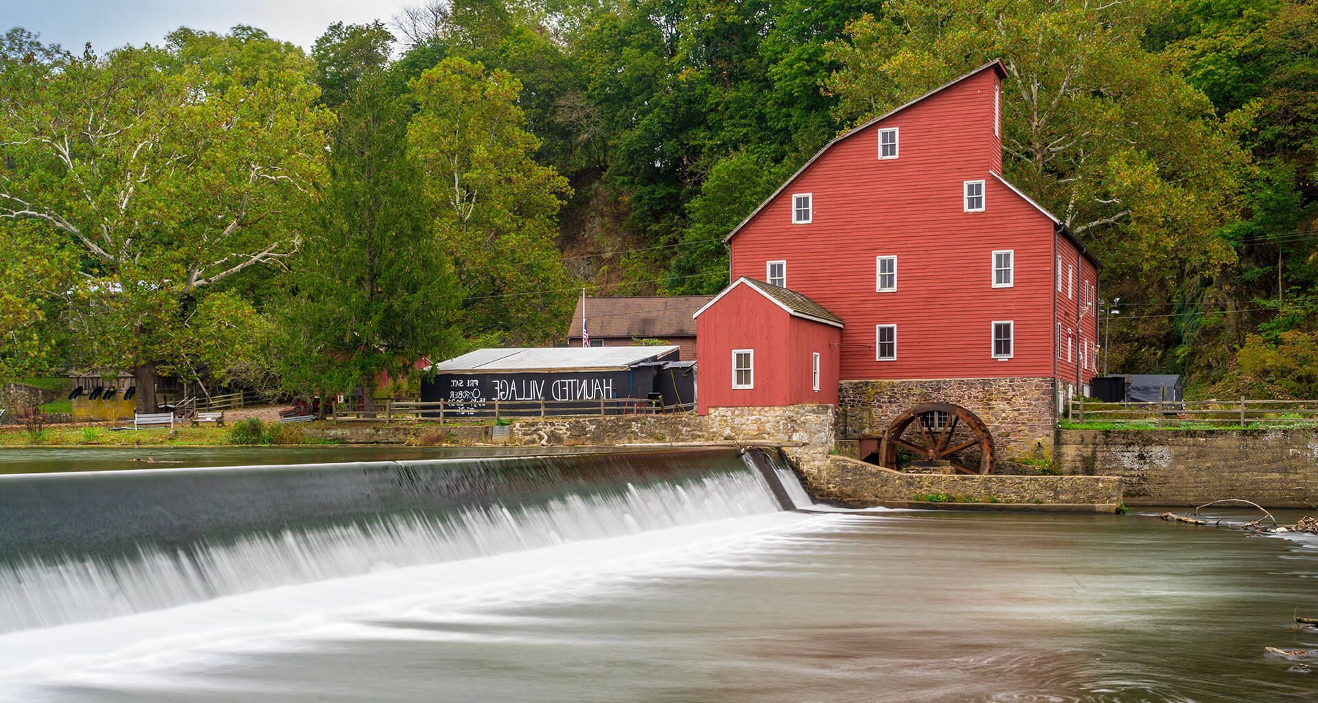 A red barn is next to a waterfall and a river.