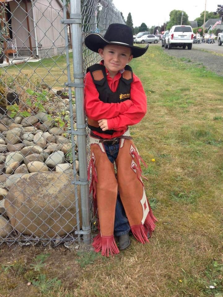Young boy in cowboy attire leans on a fence, red shirt, chaps, black hat | Genesis Automotive and RV Repair