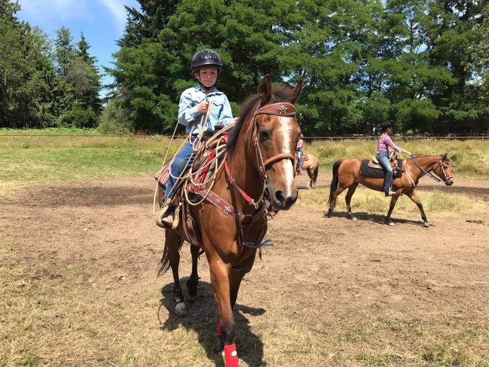 Boy riding a brown horse, holding reins, another rider in the background. Outdoors, sunny day | Genesis Automotive and RV Repair