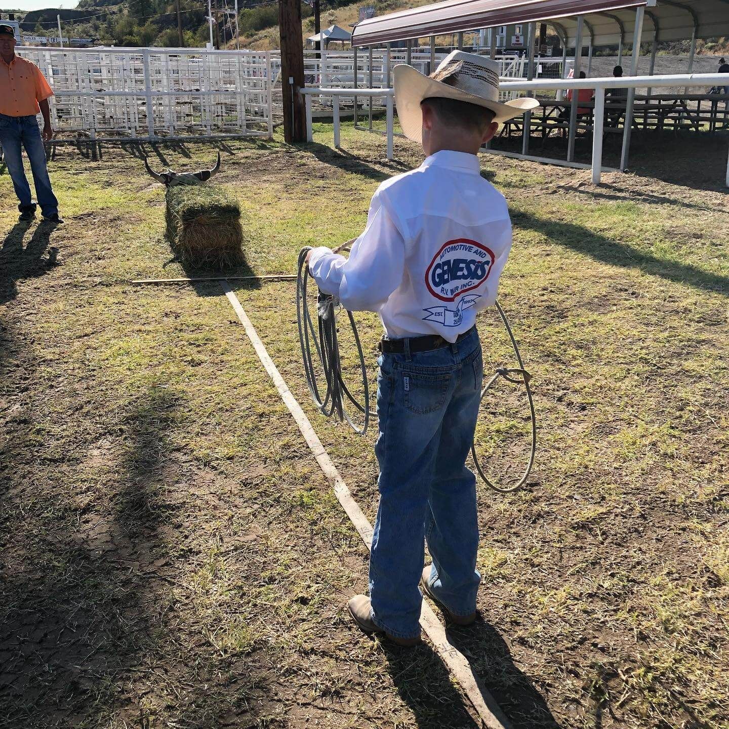 Boy in cowboy attire roping hay bale in outdoor arena; sunlight | Genesis Automotive and RV Repair