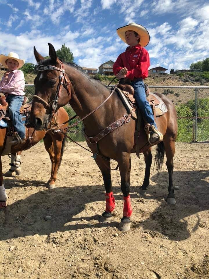 Boy in cowboy hat and red shirt on a brown horse, with another rider nearby | Genesis Automotive and RV Repair
