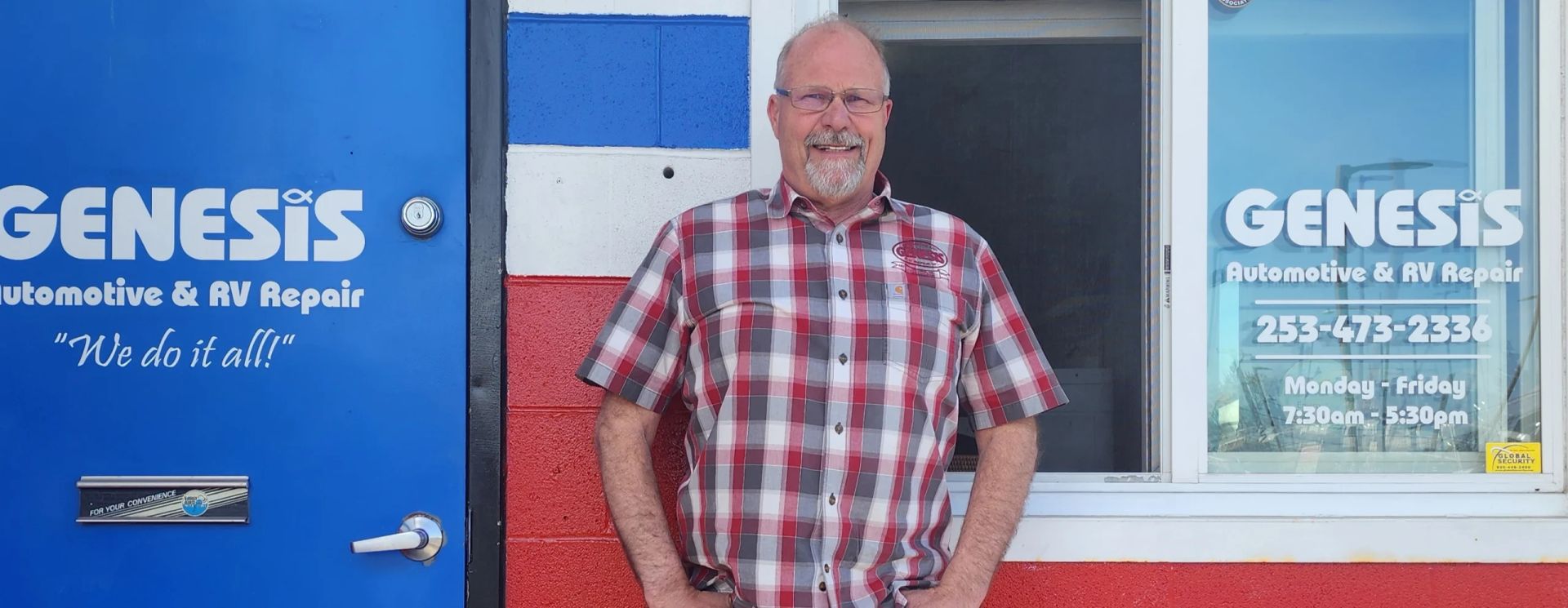 Man in plaid shirt standing in front of a blue-doored auto shop, "Genesis" sign visible | Genesis Automotive and RV Repair