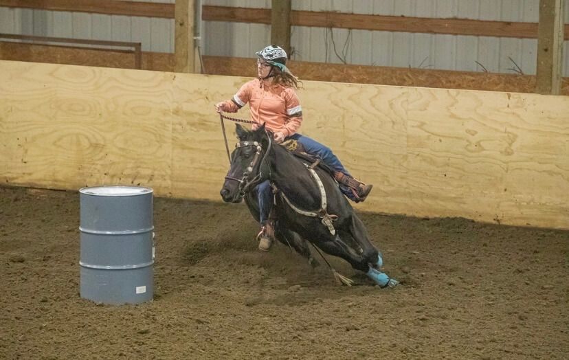 Woman on black horse in barrel racing competition, indoor arena | Genesis Automotive and RV Repair
