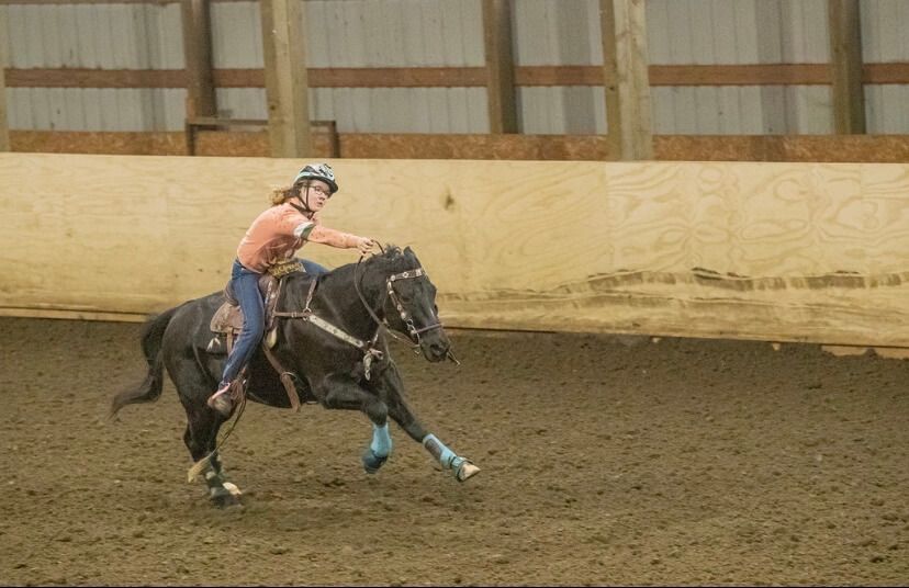 Woman on black horse racing barrels in an indoor arena, wearing helmet and western attire | Genesis Automotive and RV Repair