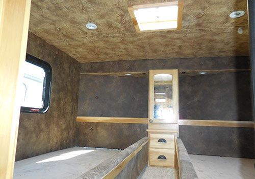 Interior of a horse trailer living quarters with a bed, closet, and window. Earth-tone walls and wooden accents | Genesis Automotive and RV Repair
