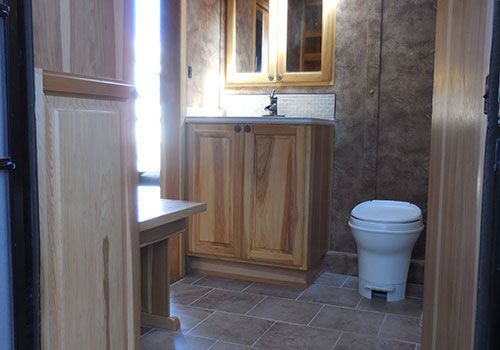 Bathroom with wooden cabinetry, a toilet, and a sink. Brown tiled floor and brown textured walls | Genesis Automotive and RV Repair