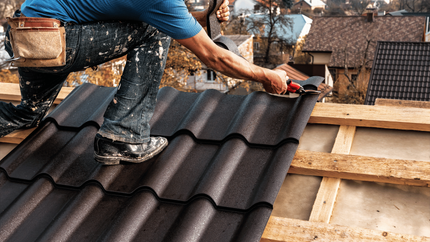 A man is kneeling on top of a roof while working on it.