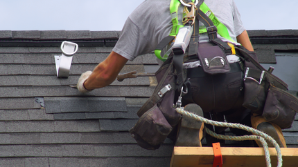 A man wearing a harness is working on a roof.