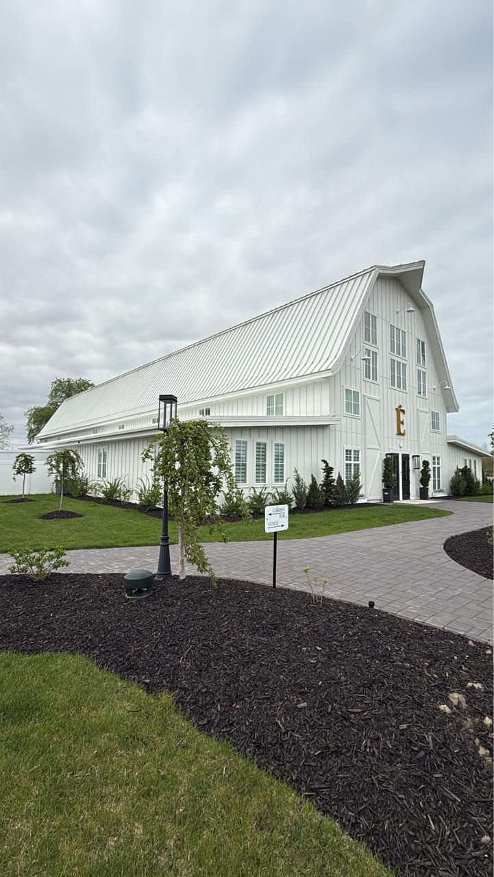 A large white barn with a metal roof is sitting on top of a lush green field.