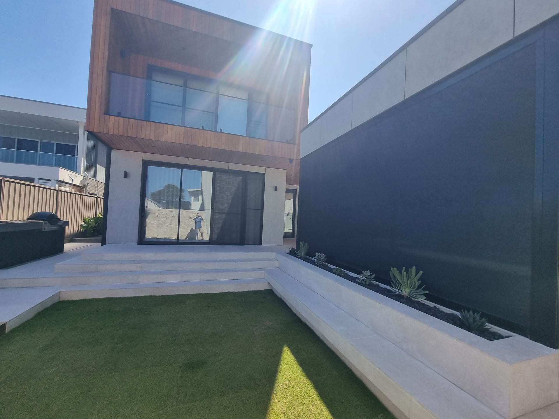 Modern house with wooden facade, glass doors, and a black privacy screen. Bright sunlight. — Glenn Koek - Shutters - Curtains - Blinds in Sutherland Shire, NSW
