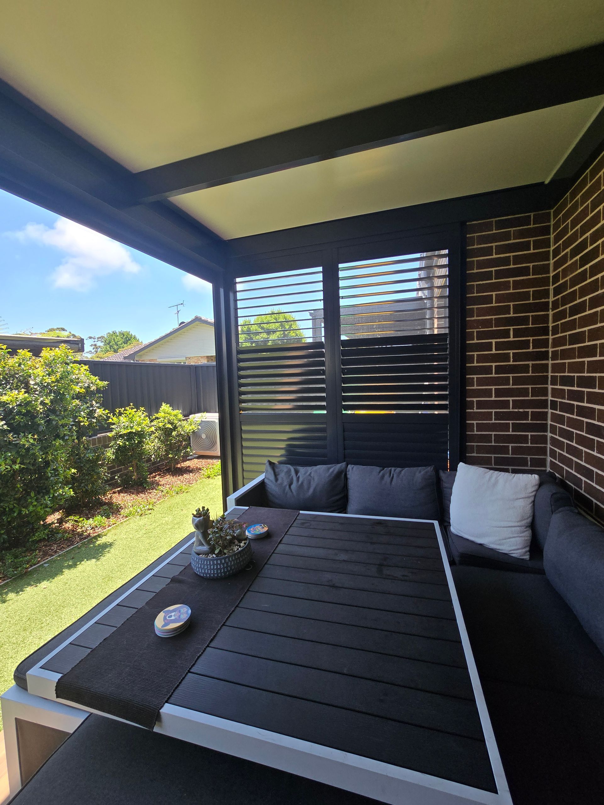 Outdoor patio with a table, seating, and brick wall; sunny day. — Glenn Koek - Shutters - Curtains - Blinds in West Wollongong, NSW