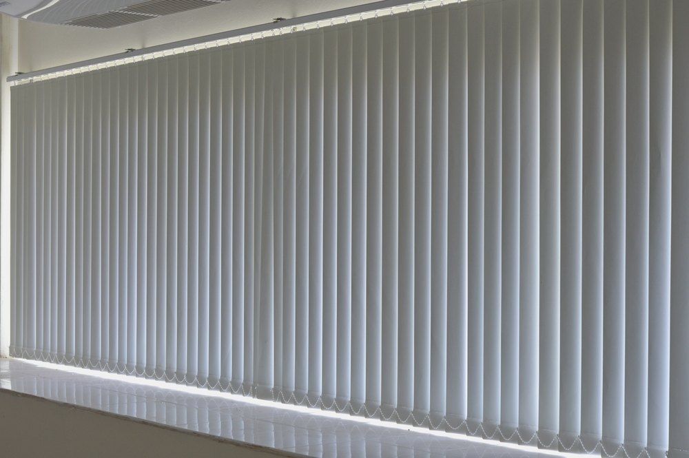 Vertical, white blinds covering a large window, providing privacy and light control in an interior setting. — Glenn Koek - Shutters - Curtains - Blinds in West Wollongong, NSW