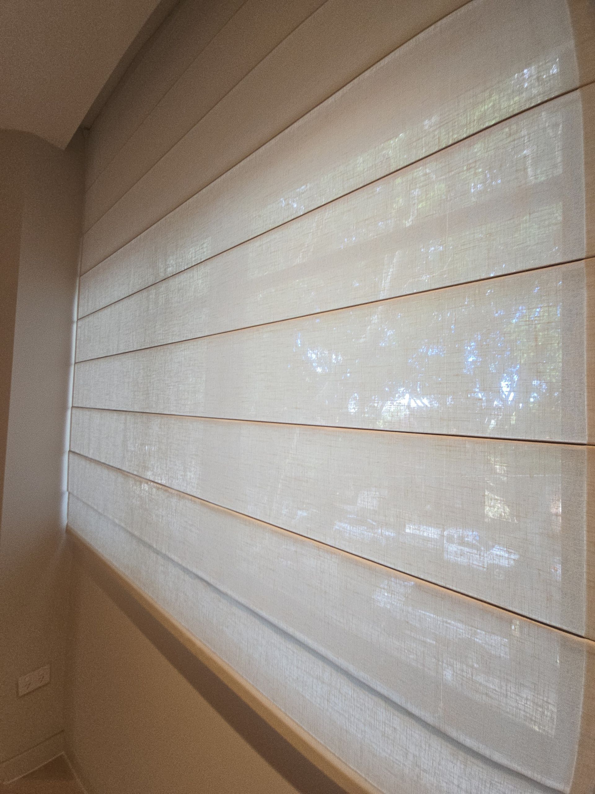 Cream-coloured Roman shade, partially lowered, covering a window in a room with beige walls. — Glenn Koek - Shutters - Curtains - Blinds in West Wollongong, NSW