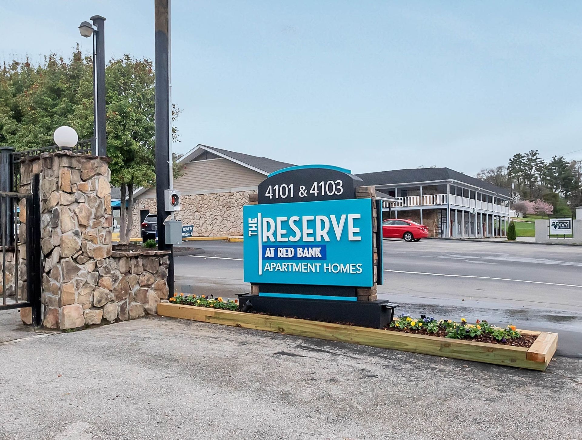 A teal sign for The Reserve at Red Bank apartment homes at 4101 & 4103, located at an entrance with stone pillars.