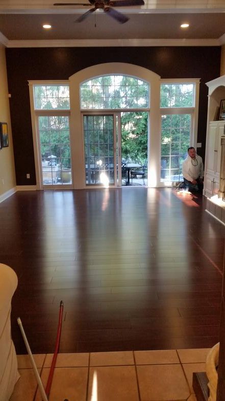 A man is kneeling on a wooden floor in a living room.
